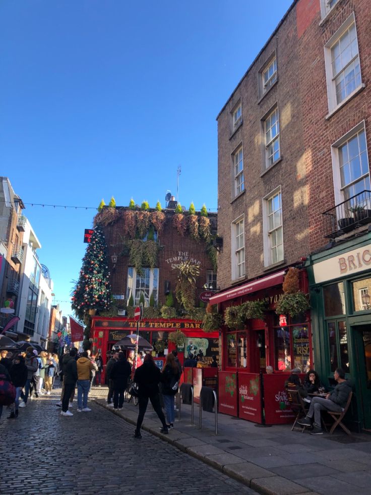 people are walking down the street in front of buildings with christmas decorations on them and hanging from the roof