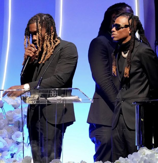 two people standing at a podium with flowers in front of them and one person wearing sunglasses