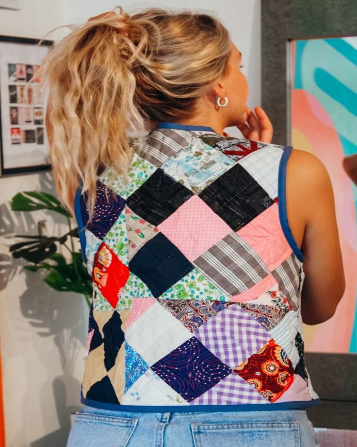 a woman standing in front of a painting looking at her cell phone and wearing a colorful top