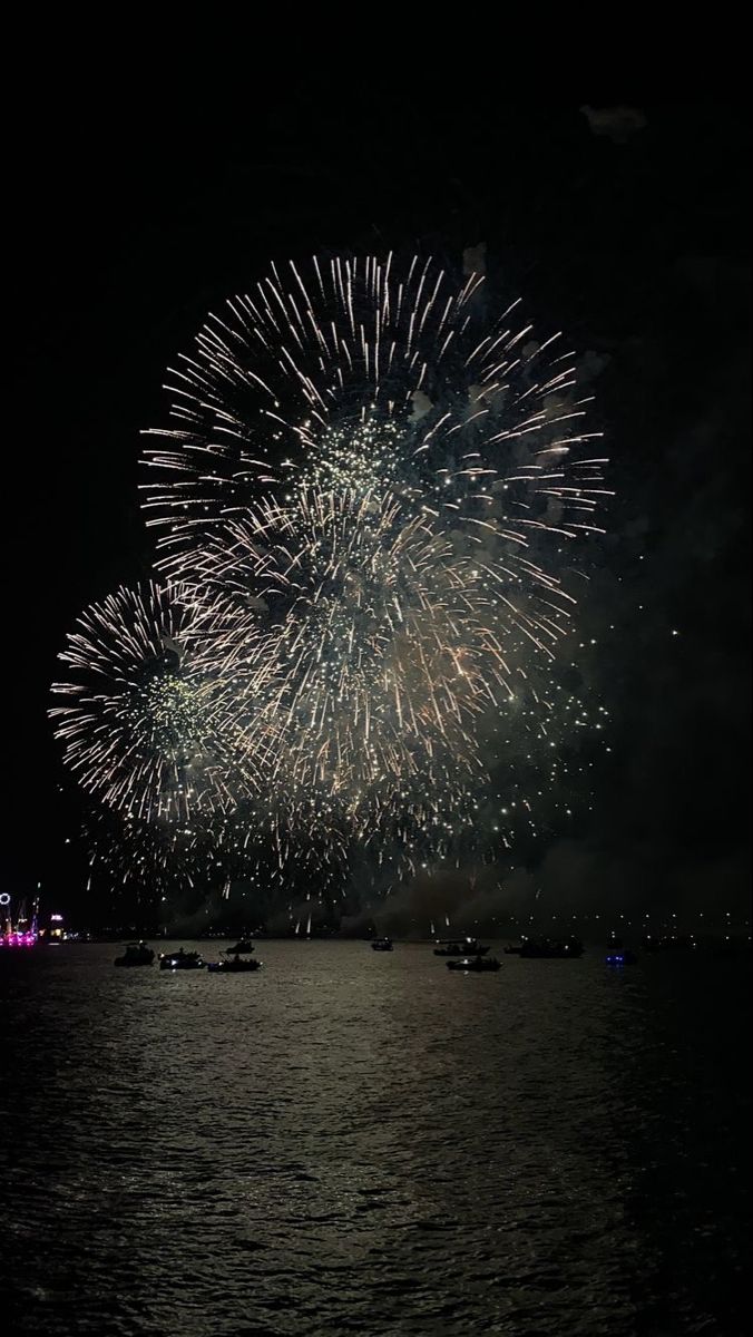 fireworks are lit up in the night sky over water with boats floating on the water