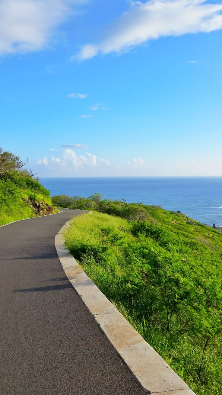 an empty road near the ocean on a sunny day with blue sky and clouds in the background