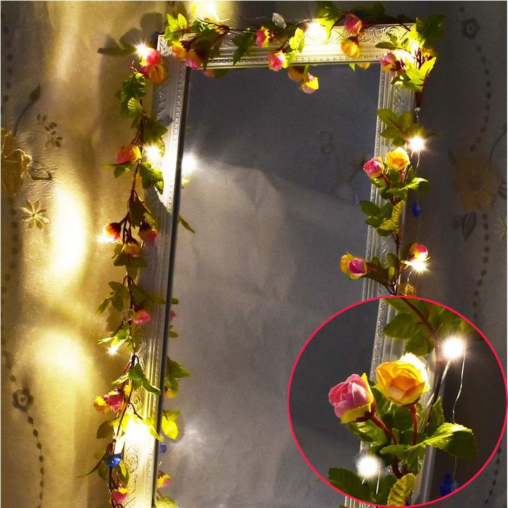 a mirror that has flowers on it and some lights around the frame in front of it