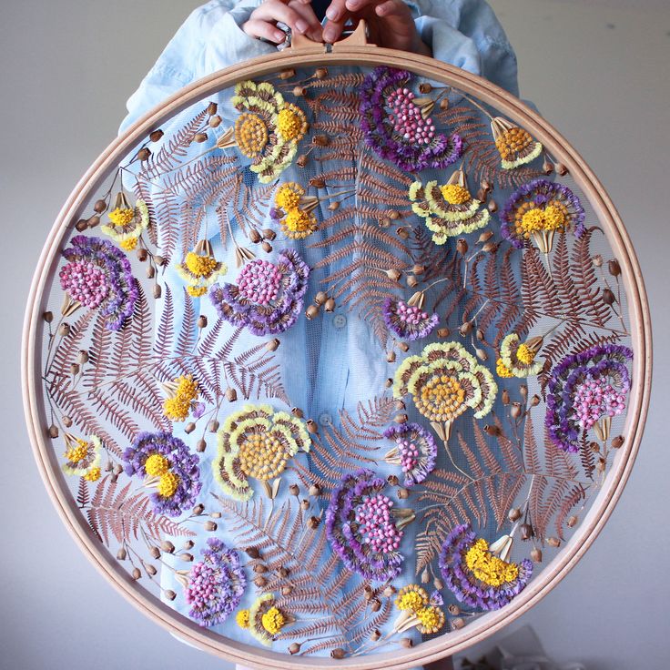 a woman is holding an embroidery project in front of her face