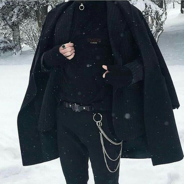 a man in black is standing in the snow with his hand on his hip and wearing a chain around his neck