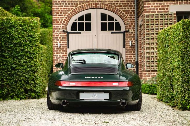 a green porsche parked in front of a brick building with an arched doorway and door