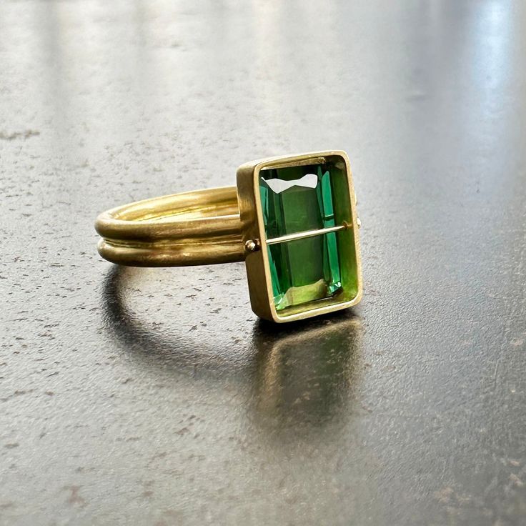 This ring lives at Danielle Shop in San Francisco. Please contact Hilary to inquire about this piece. You won't be able to take your eyes off of this radiant cut green tourmaline ring. Aptly named, this stone radiates an array vibrant green hues. The double band compliments the crossbar and provides a luxurious contrast to the stone's geometric and longitudinal facets. A true one of a kind. 18k gold. 2.42 carat radiant cut green tourmaline. Size 7. Modern Green Emerald-cut Jewelry, Green Tourmaline Ring For May Birthstone, Radiant Cut Green Emerald Ring, Modern Radiant Cut Emerald Jewelry, Modern Tourmaline Emerald Cut Rings, Modern Tourmaline Rings With Emerald Cut, Fine Jewelry Green Emerald Cut Emerald Ring, Modern Tourmaline Rings In Emerald Cut, Fine Jewelry Green Emerald Cut Ring