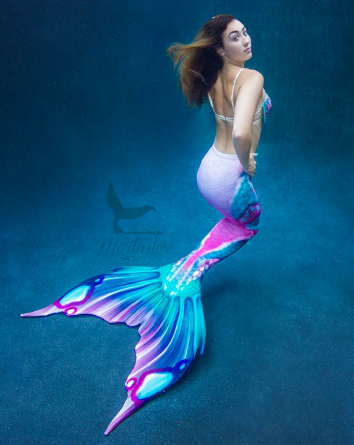 a woman is sitting on the bottom of a mermaid tail while holding her hands behind her back