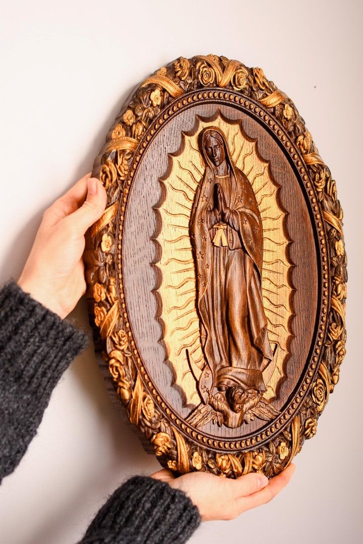 a person holding up a wooden plaque with the image of virgin mary on it's face