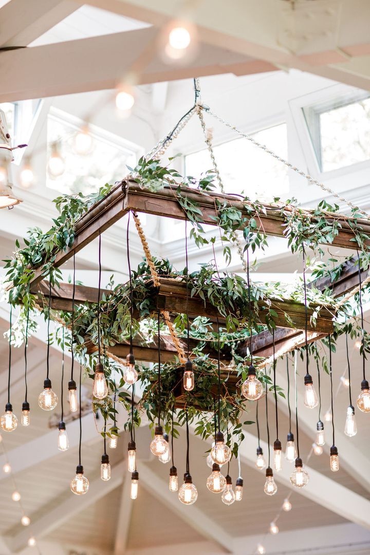 a chandelier with lots of lights hanging from it's sides and greenery on the ceiling