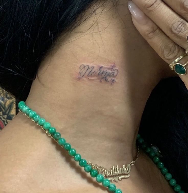 a woman with a name tattoo on her neck and behind her is a green beaded necklace