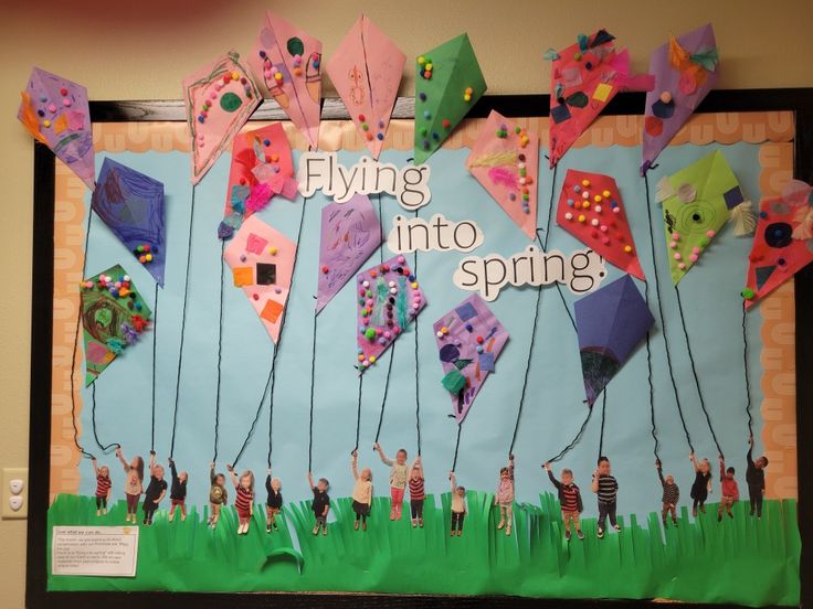 a bulletin board with some kites hanging from it's sides and the words flying into spring