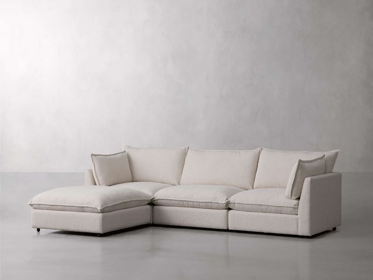 a white sectional sofa with pillows on the top and bottom, in front of a gray wall