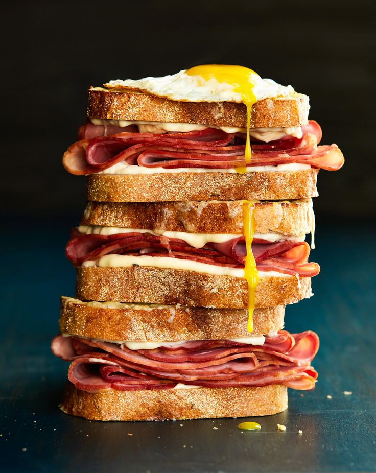 a stack of sandwiches with ham, cheese and an egg being drizzled on top