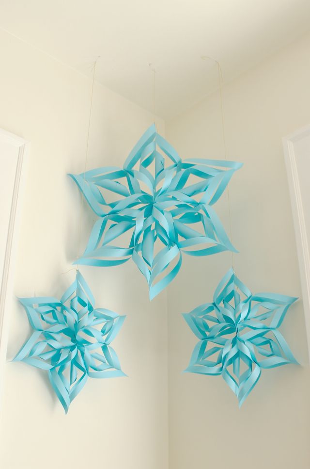 three blue paper snowflakes hanging from the ceiling in a room with white walls