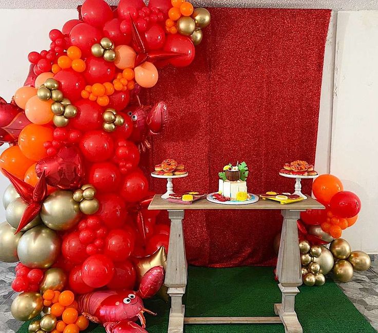 a table topped with lots of balloons next to a tall red and gold balloon tree