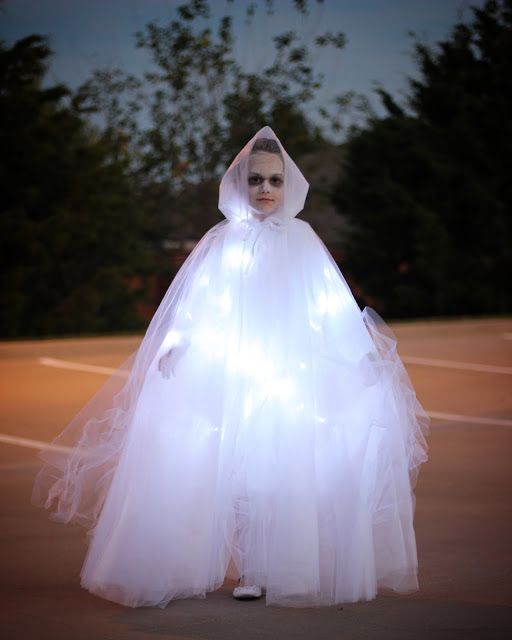 a woman dressed as a ghost standing on a tennis court at night with lights in her hands