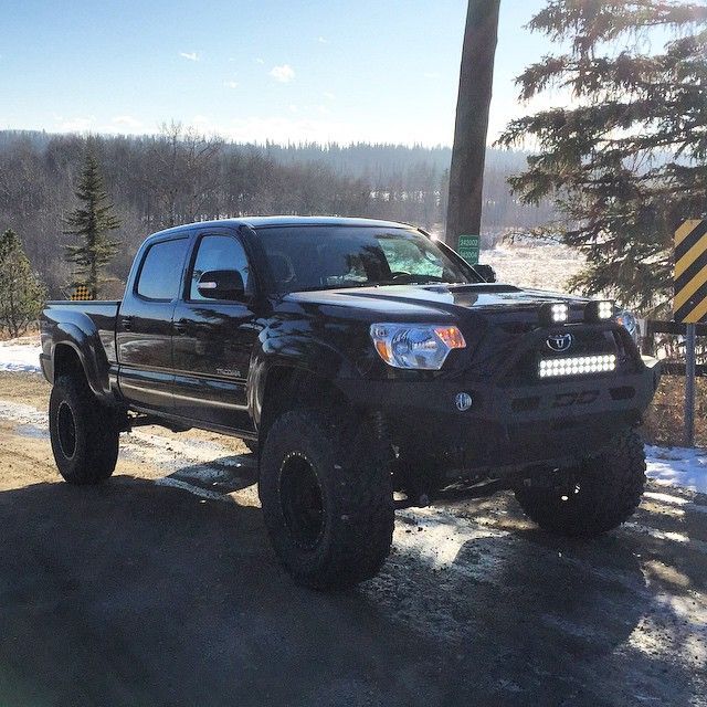 a black truck parked on the side of a dirt road next to trees and snow