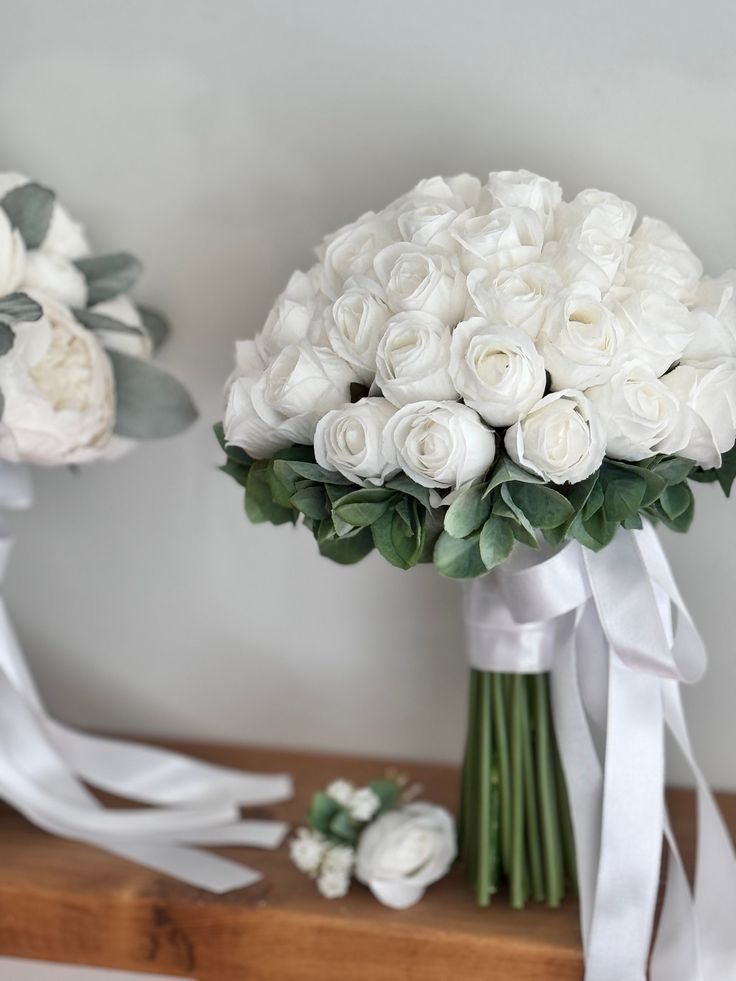 two bouquets of white roses and greenery sit on a shelf next to each other