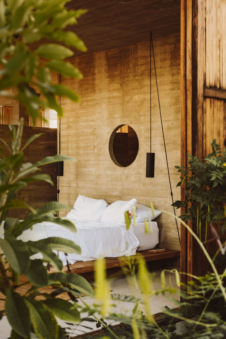 a bed sitting in the middle of a bedroom next to a wooden wall and plants