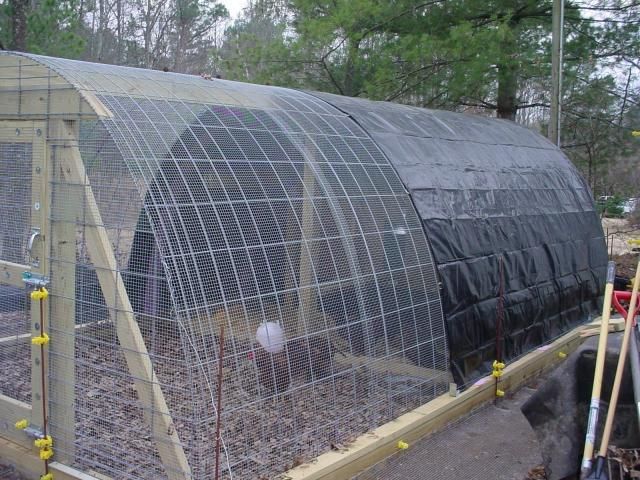 a large green house filled with lots of plants and dirt in the middle of a yard