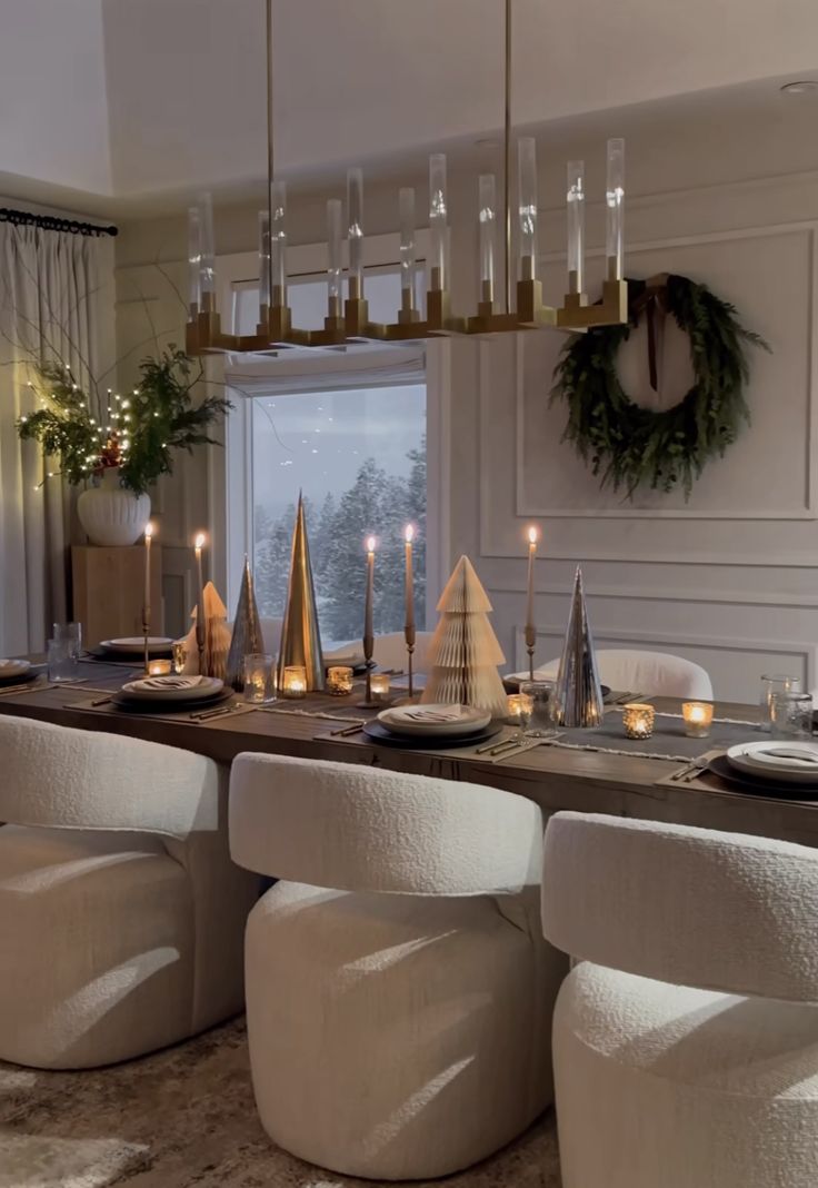 a dining room table set for christmas with candles and decorations on the table, surrounded by white chairs