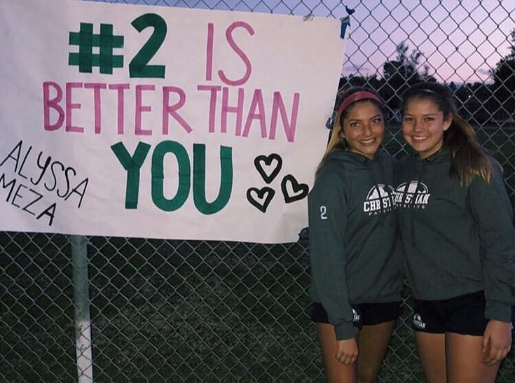 two girls standing in front of a fence with a sign that says 2 is better than you