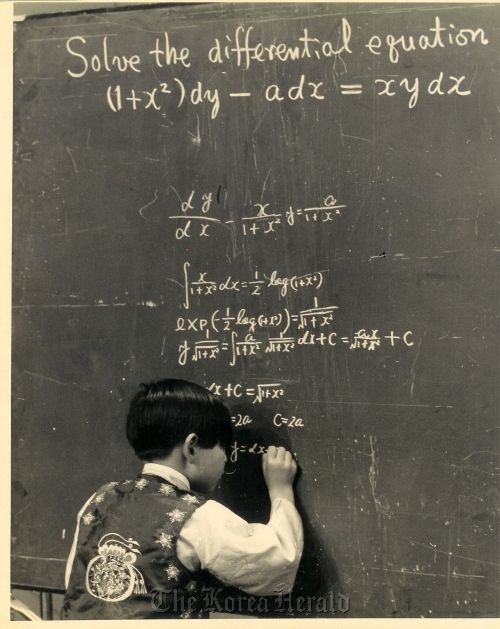 a young boy writing on a blackboard in front of a chalkboard with calculations