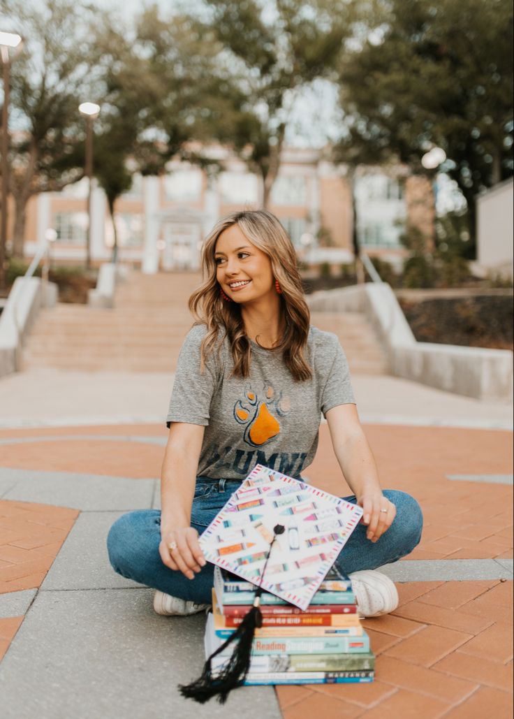 a woman is sitting on the ground with her books in front of her and smiling