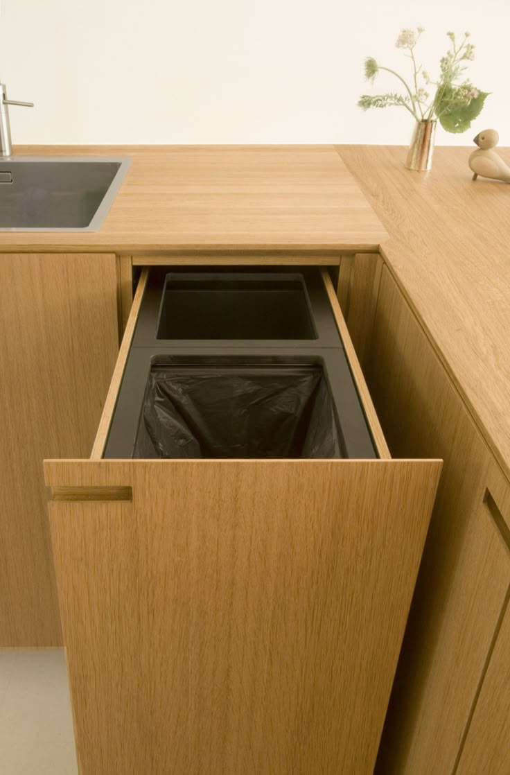 a wooden cabinet with a black trash can in the bottom drawer and a sink behind it