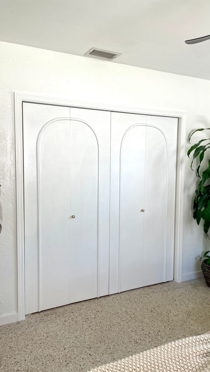 an empty room with two white doors and a potted plant on the floor next to it