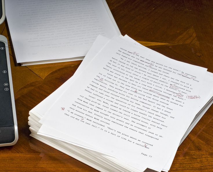 a pile of papers sitting on top of a wooden table next to a cell phone