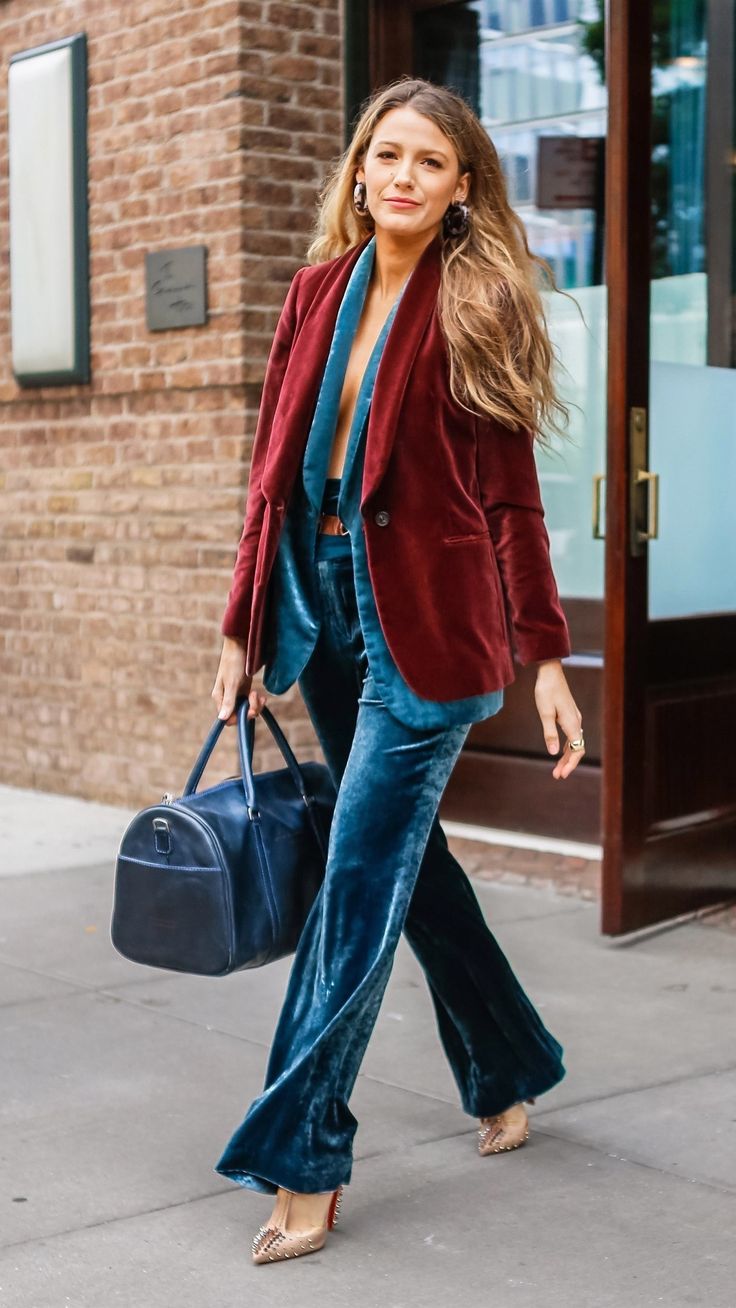 a woman walking down the street carrying a handbag and wearing a red velvet blazer