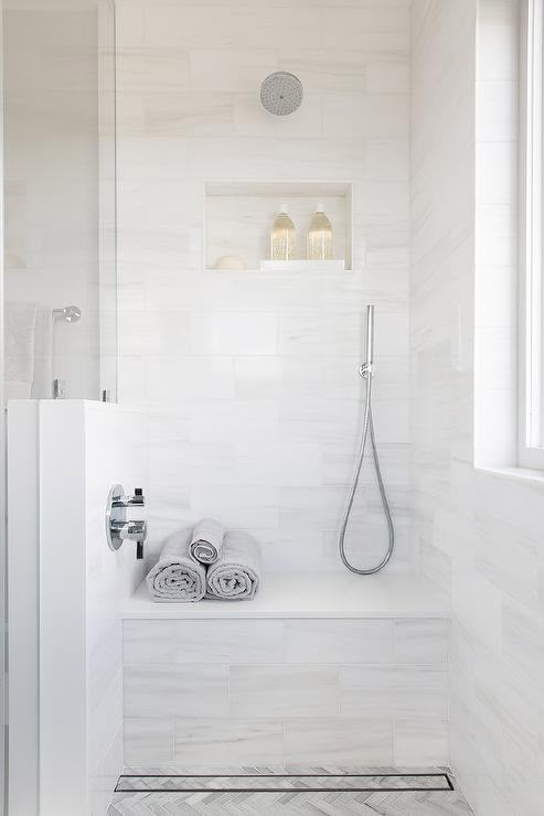 a bathroom with white walls and flooring has a shower head, towel rack, and window