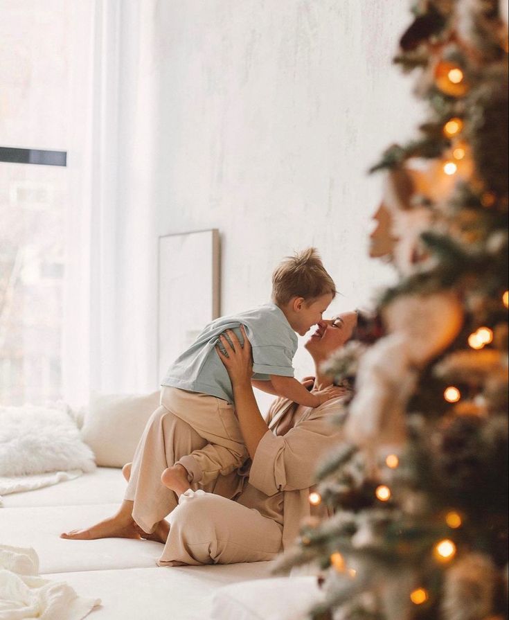 a woman sitting on the floor next to a christmas tree with a baby in her lap