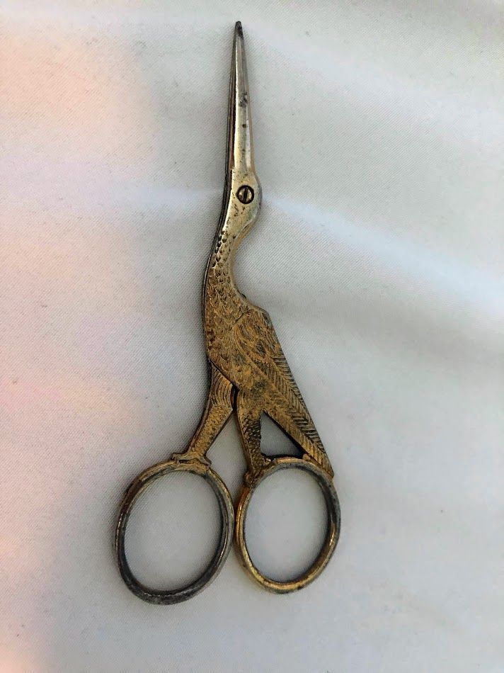 an old pair of scissors sitting on top of a white cloth covered table with a black handle