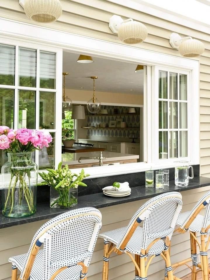 a bar with four chairs and vases on the counter in front of an open window