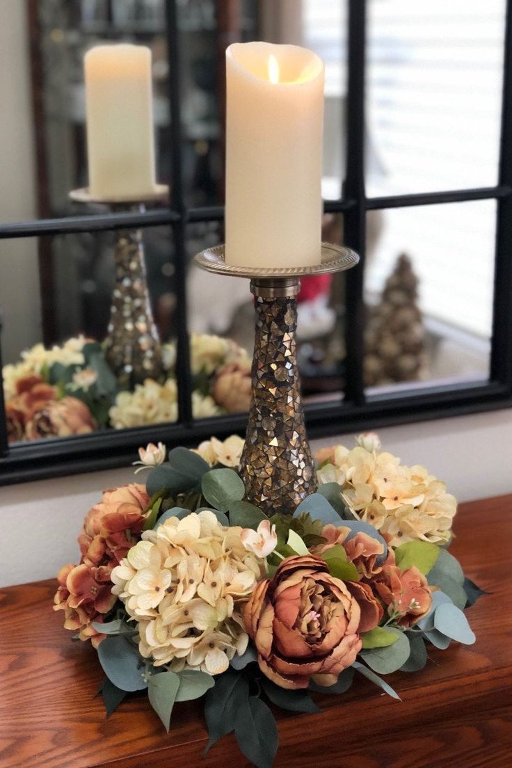 there is a candle that is sitting on the table with flowers in front of it