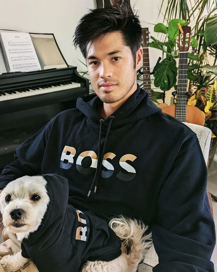 a man sitting in front of a piano holding a small dog wearing a hoodie