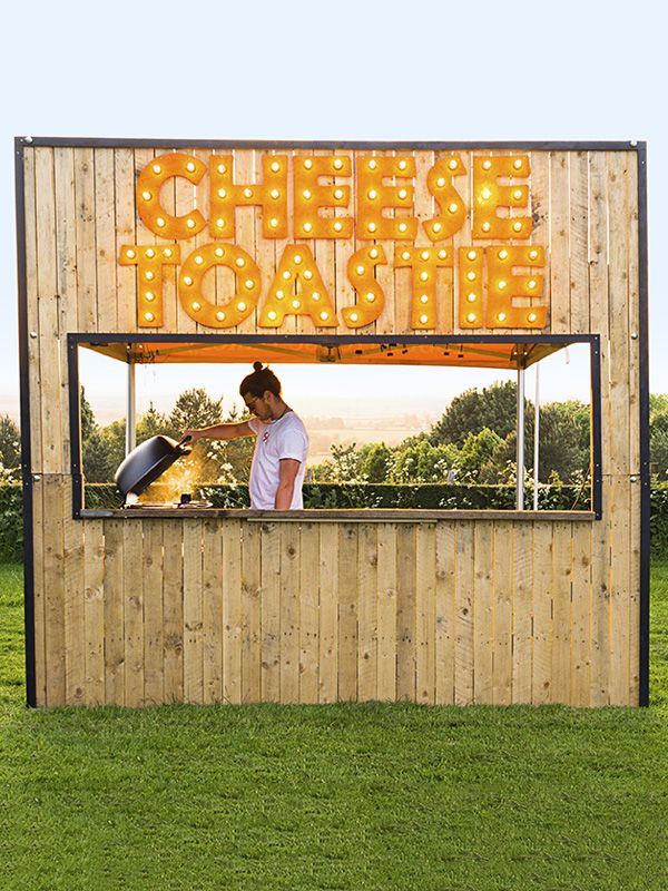 a person standing behind a food stand with lights on it's sides and the words cheese toastie above them