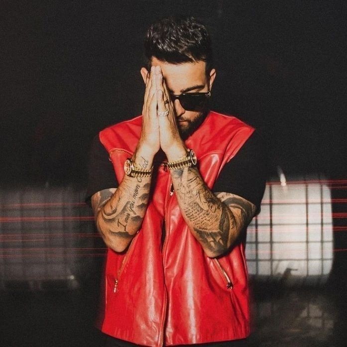 a man in a red leather vest covers his face with his hands while standing against a black background