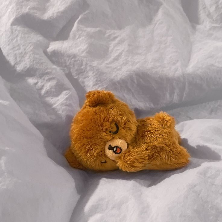 a brown teddy bear laying on top of white sheets