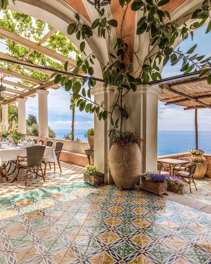 an outdoor dining area overlooking the ocean with tables and chairs, potted plants on either side