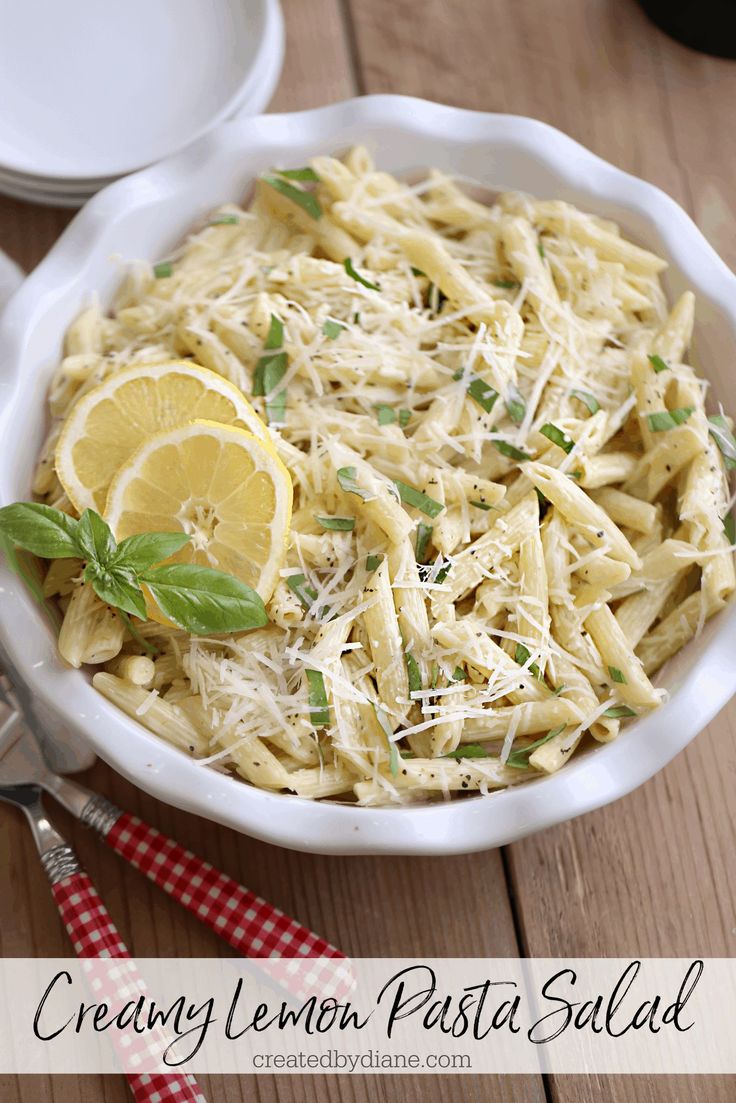 a white bowl filled with pasta and topped with lemon slices, parmesan cheese and basil