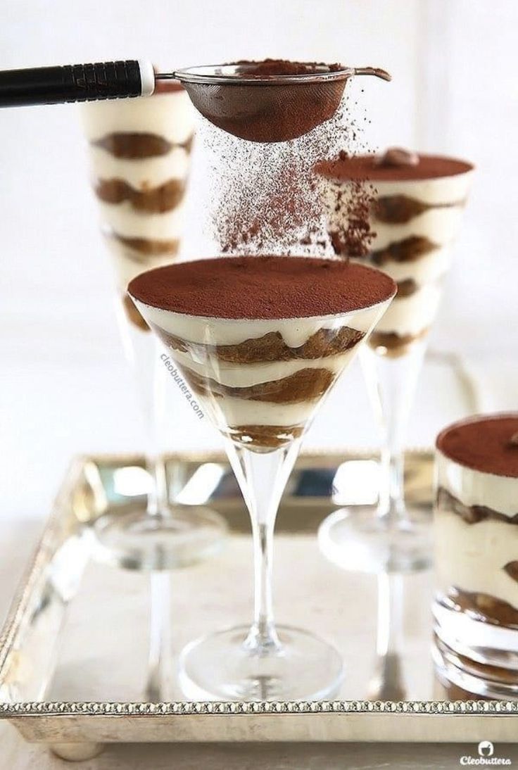 four desserts in glasses on a tray, with one being sprinkled with chocolate