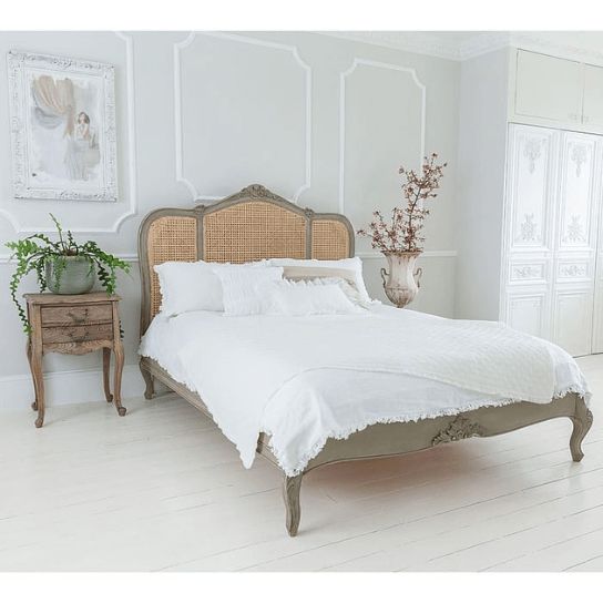 a bed with white sheets and pillows in a room next to a plant on the floor