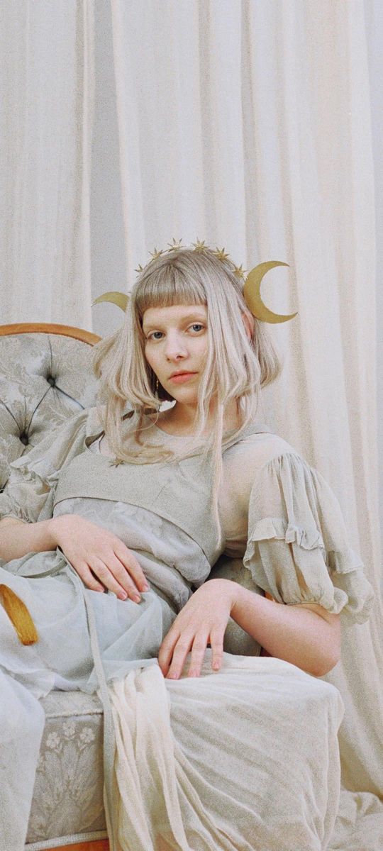 a woman with blonde hair sitting in a chair wearing a white dress and gold horns