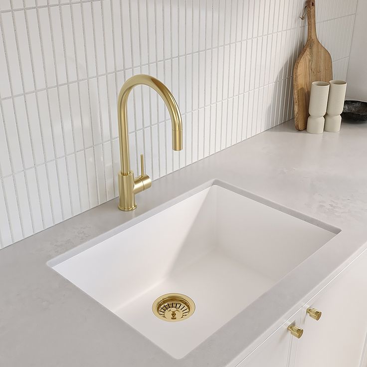 a white kitchen sink sitting under a faucet next to a wooden cutting board