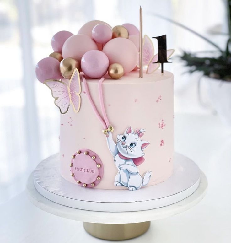 there is a pink cake with gold decorations on the top, and a cat decoration on the bottom