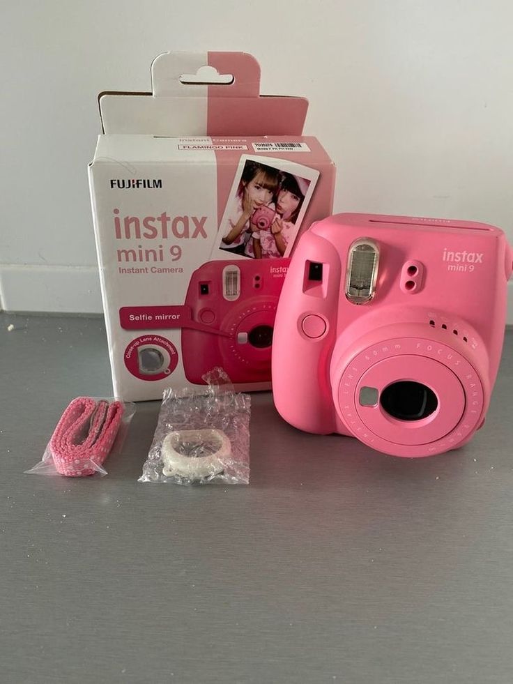 a pink camera sitting on top of a table next to a box and other items