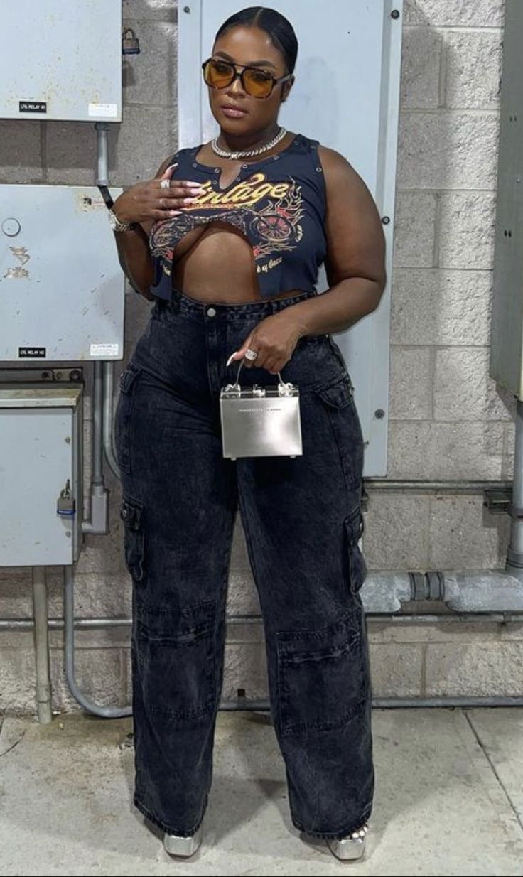 a woman standing in front of a white wall holding a silver purse and looking at her cell phone